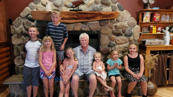 Gary surrounded by his grandchildren in front of a stone fireplace